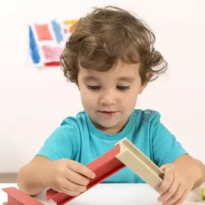 Criança a brincar com peças de construir vermelhas e bege numa mesa branca