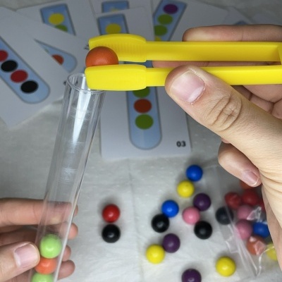 Jogo educativo com bolas coloridas, pinça amarela, tubo transparente e cartões com padrões coloridos