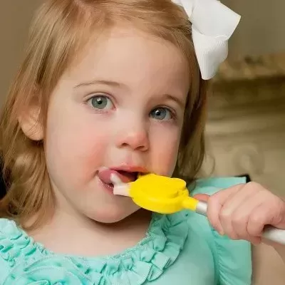 Menina pequena a usar escova de dentes infantil amarela