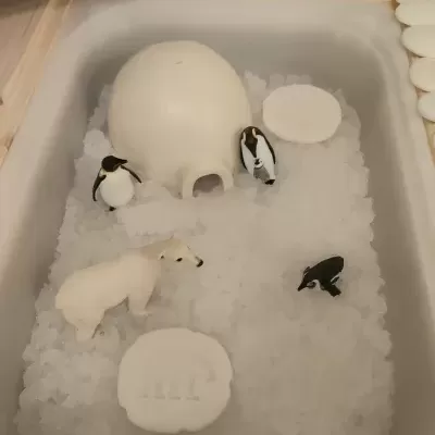 Banheira com iglu e animais de plástico sobre gelo artificial