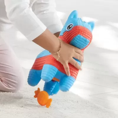 Brinquedo de animal azul e vermelho com textura acolchoada numa mão de criança e brinquedo laranja em forma de doce no chão.