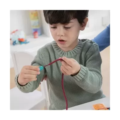 Criança com suéter verde segurando cabo vermelho com ponta azul em ambiente interno claro