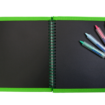 Caderno preto com margem verde e canetas coloridas sobre fundo branco