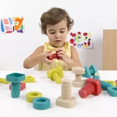 Menina a brincar com parafusos e porcas de madeira coloridos numa mesa branca