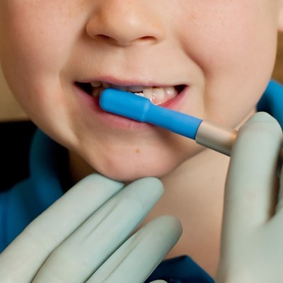 Criança com peça azul na boca e mão enluvada a segurar