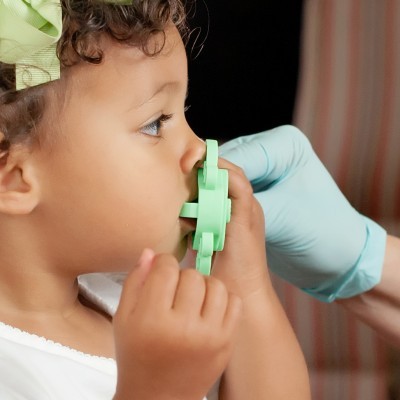 Criança usa inalador verde com auxílio de mão com luva médica azul