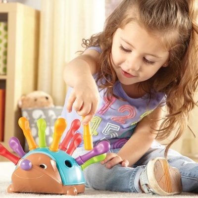 Menina a brincar com brinquedo em forma de ouriço colorido no chão