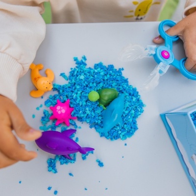 Criança a brincar com areia cinética azul e brinquedos de plástico coloridos sobre mesa branca