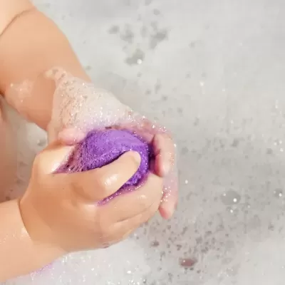 Mãos de criança a segurar bola roxa com espuma de sabão