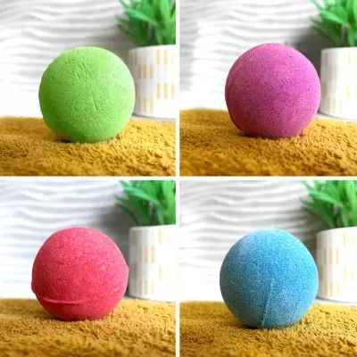 Bolas de banho coloridas em verde, roxo, vermelho e azul sobre superfície amarela com planta ao fundo