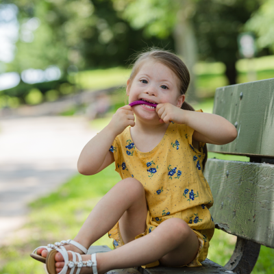 Criança a brincar sentada num banco no parque com roupa amarela floral e sandálias brancas