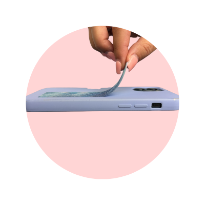 Telemóvel com capa lilás e mão a levantar autocolante no centro do ecrã, fundo rosa