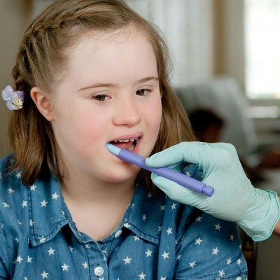 Criança a realizar exame oral com instrumento azul por profissional com luva médica.
