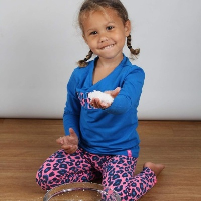 Criança com roupa colorida segurando tigela e substância branca sentada no chão de madeira