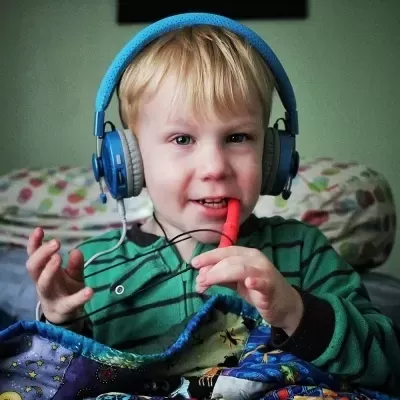 Criança com auscultadores azuis a tocar flauta vermelha