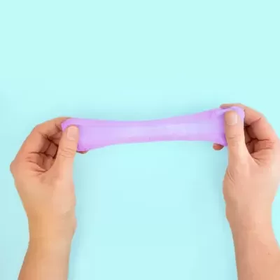 Brinquedo de slime cor-de-rosa esticado por duas mãos sobre fundo azul