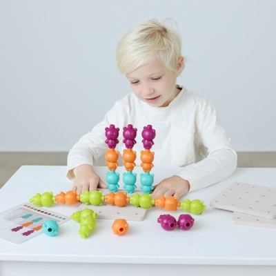 Menino loiro sentado brincando com peças coloridas em forma de animais sobre mesa branca