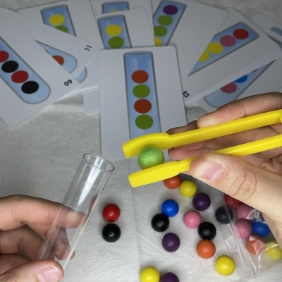 Jogo de lógica com bolas coloridas, cartões com padrões e mãos a usar pinça amarela