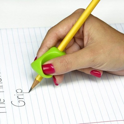 Mão segurando um lápis com acessório verde escreve em papel pautado
