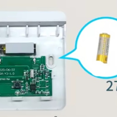 Placa eletrónica verde dentro de caixa branca com bateria amarela mostrada em destaque