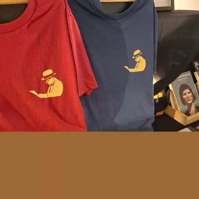 Dois T-shirts vermelha e azul com estampa amarela de figura a ler, e livros ao lado em mesa