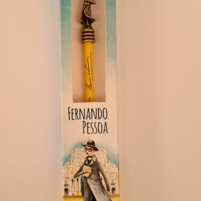 Caneta amarela com figura metálica no topo em caixa decorativa com ilustração de Fernando Pessoa.