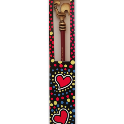 Caneta vermelha com tampa dourada em forma de galo numa caixa preta com pontos coloridos e corações