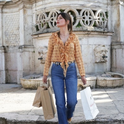 Mulher com camisa laranja e calças de ganga a descer escadaria junto a fonte de pedra