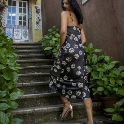 Mulher usando vestido preto com espirais brancas e salto alto dourado a subir escadas exteriores