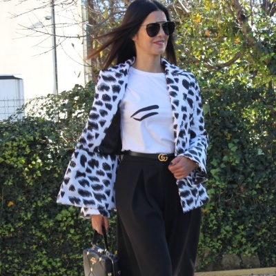 Mulher longa com casaco branco e preto, t-shirt branca, calças pretas e acessórios pretos ao ar livre