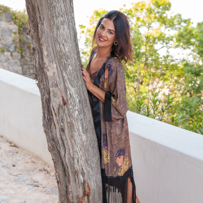 Mulher com quimono castanho e vestido preto junto a uma árvore no exterior