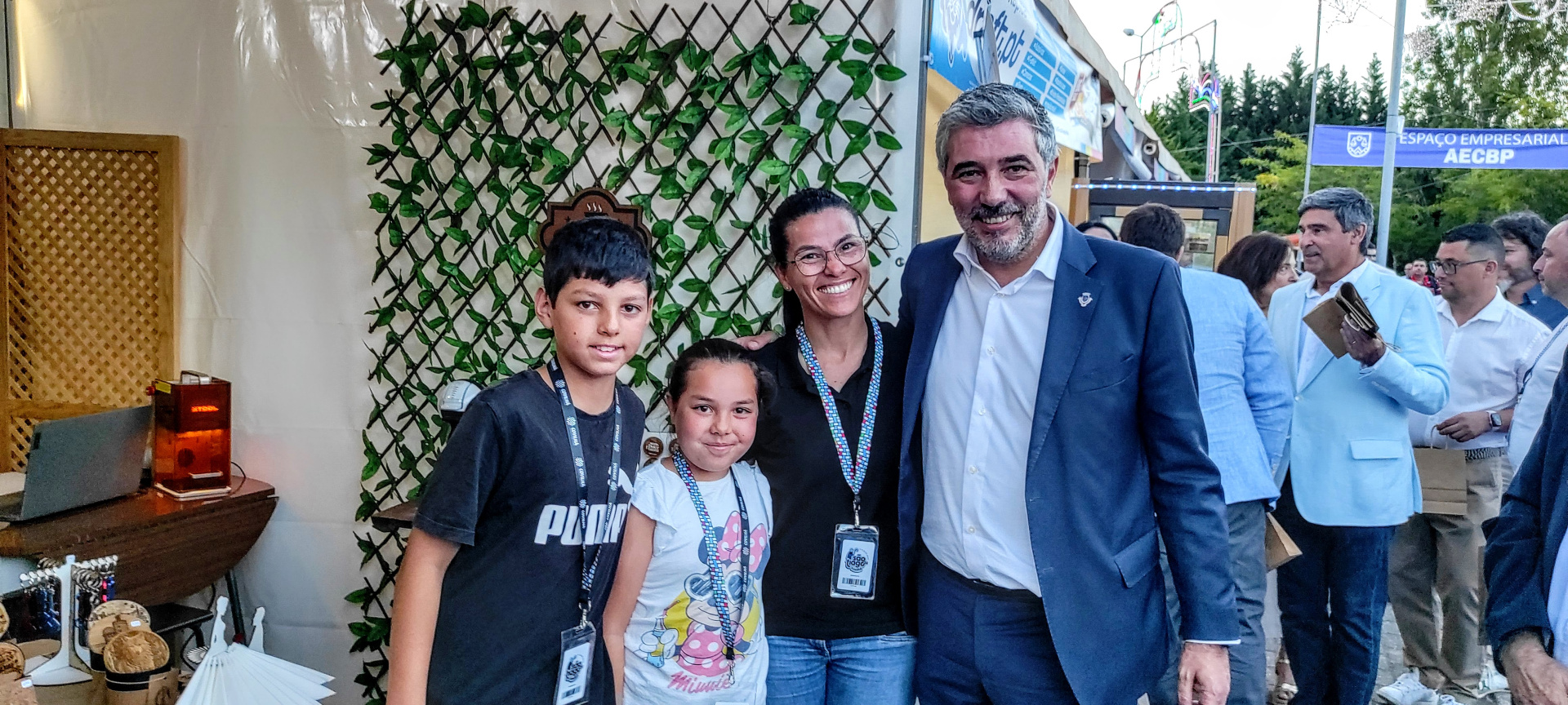 Quatro pessoas posando em feira com roupas casuais e um fato azul, e banner azul ao fundo.