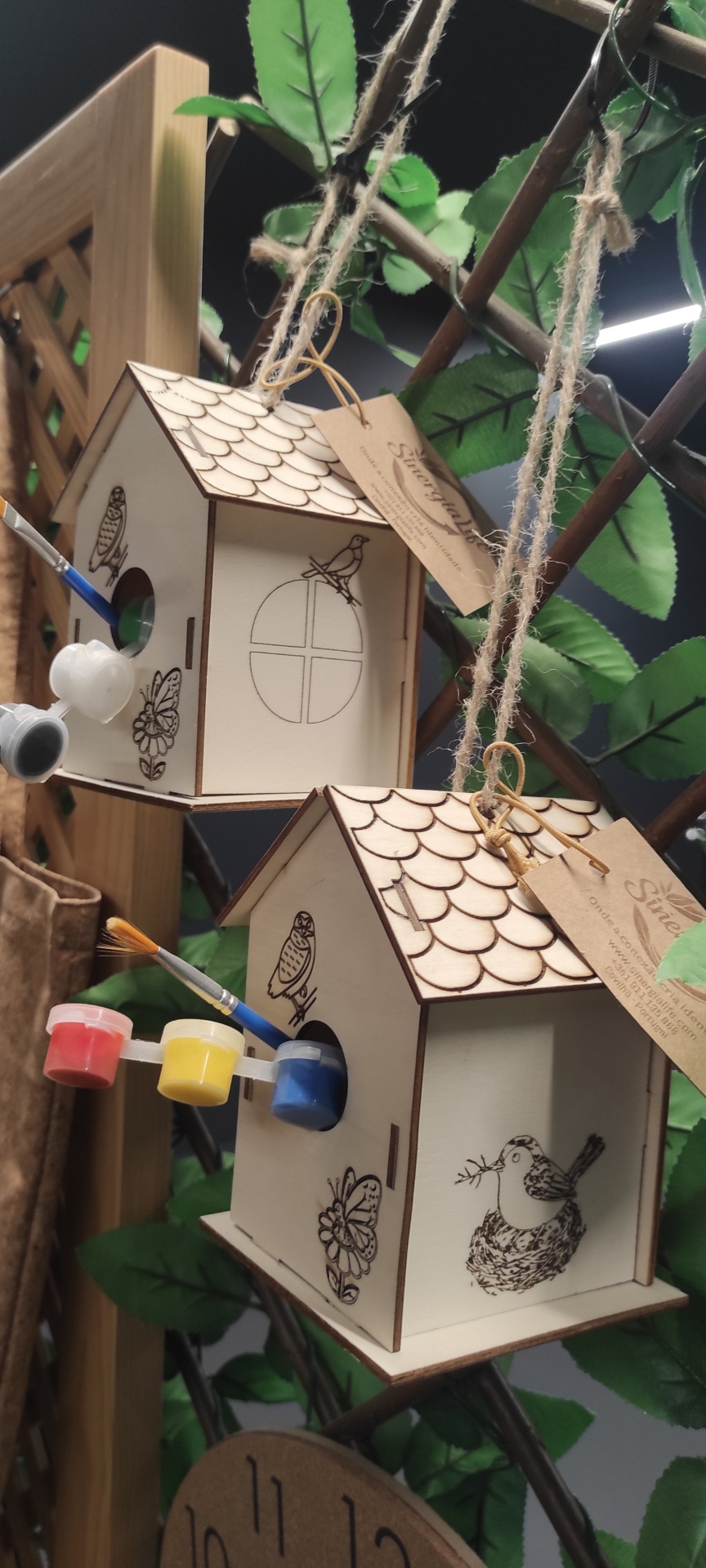 CASINHA DE PASSARINHO Casas de madeira penduradas com desenhos para pintar, tintas e pincéis à vista.