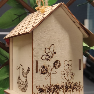 Casinha pendurada de madeira clara com desenhos decorativos e corda para pendurar