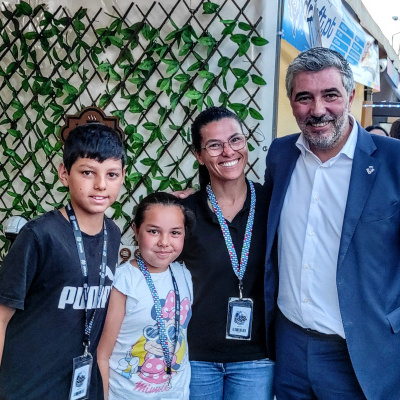 Quatro pessoas posando em feira com roupas casuais e um fato azul, e banner azul ao fundo.