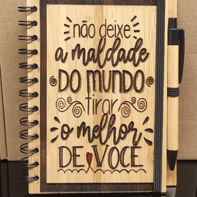 Caderno de madeira clara com texto gravado e caneta preta