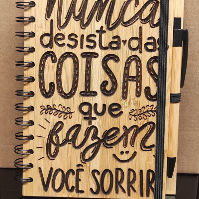 Caderno de madeira com texto gravado e caneta presa ao lado