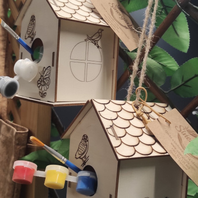 Casas de madeira penduradas com desenhos para pintar, tintas e pincéis à vista.