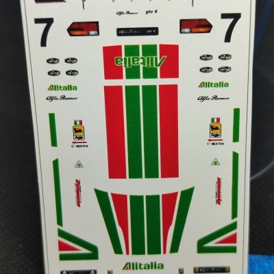 Folha de autocolantes Hot Wheels Alfa Romeo GTV Alitalia com diversos gráficos coloridos e texto, sobre fundo branco e régua metálica para escala.