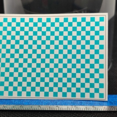 Cartão com padrão quadriculado azul e branco apoiado sobre régua metálica em fundo preto e azul