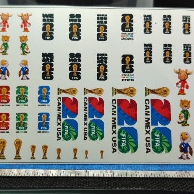 Folha branca com autocolantes FIFA World Cup 2026 com mascotes, troféu e texto em várias cores.