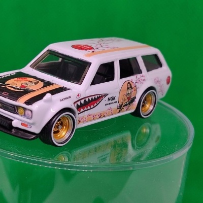 Miniatura de carro Datsun branco com decalques e rodas douradas.
