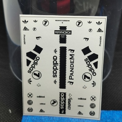 Folha branca com decalques pretos adidas, números 7, PANDEM, COOPERS, MINI LOOPER, HELLA, símbolos gráficos e régua de 6 cm à base.