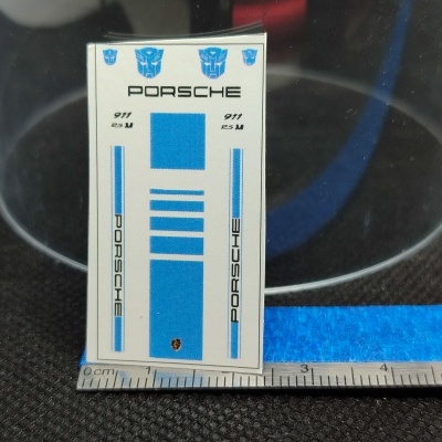 Adesivo para modelo Porsche 911 RS com logotipos azuis e texto sobre superfície preta com régua