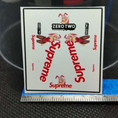 Adesivo branco com texto Supreme e Zero Two em fundo preto com régua