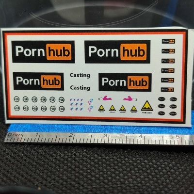Folha de decalques com logótipos e símbolos variados da marca Pornhub sobre superfície preta e régua metálica.