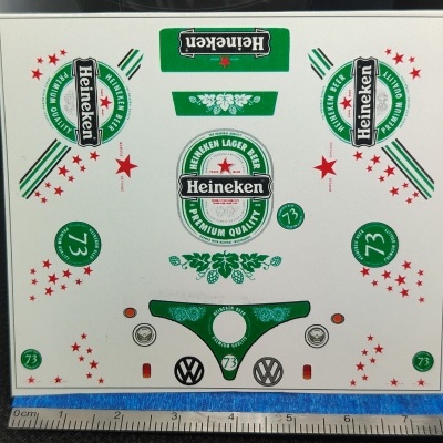 Folha com autocolantes da marca Heineken em diversas formas e cores, com régua ao lado.