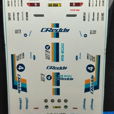 Folha de decalques para modelo Hot Wheels Ford RS200 com vários gráficos e texto em azul, laranja e branco