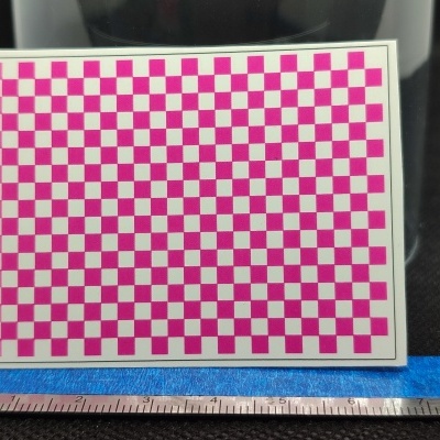 Cartão com padrão quadriculado rosa e branco apoiado numa régua sobre superfícies preta e azul