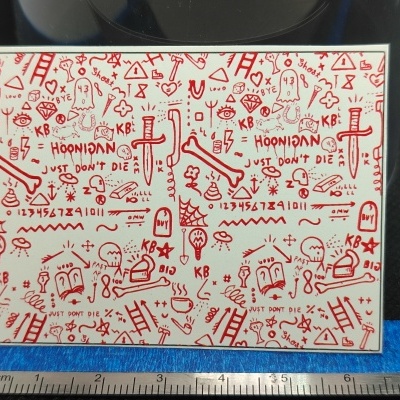 Superfície branca coberta com desenhos vermelhos variados e texto, com régua e pano azul na base.